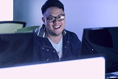 在昏暗的教室里，一位威斯康星大学的学生微笑着使用电脑.